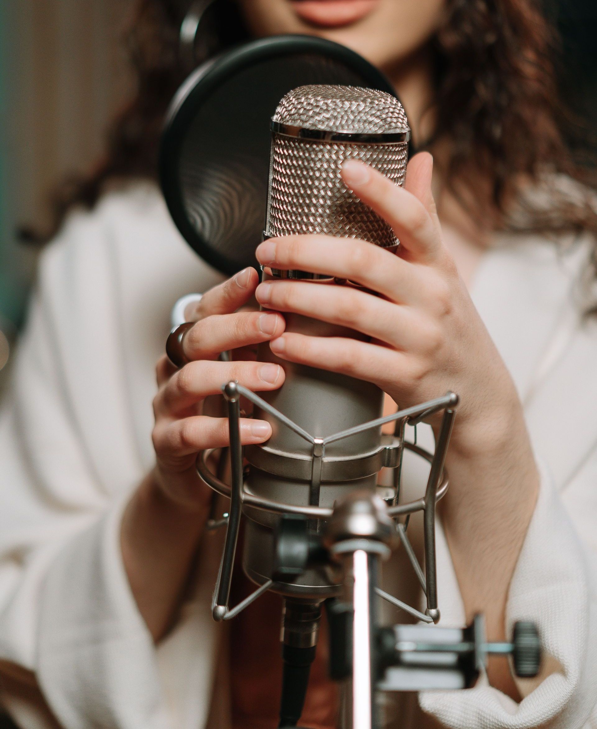 Close-up of a woman singing into a condenser microphone in a recording studio.